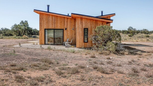 Eine moderne Holzhütte mit einem großen Schiebeglastür, einem kleinen Fenster und einem Stuhl davor.