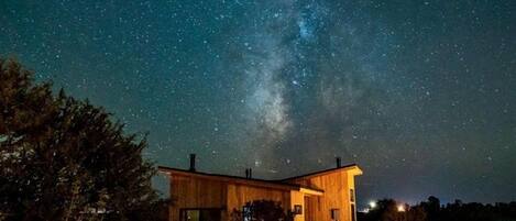A wooden cabin under a starry night sky with the Milky Way visible.