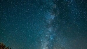 Eine Holzhütte unter einem Sternenhimmel, die Milchstraße ist sichtbar.