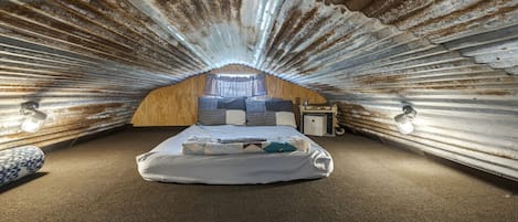 An attic bedroom with a sloped ceiling, a bed with pillows, a nightstand, and two wall-mounted lamps.