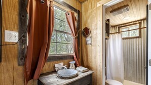 Une salle de bain rustique avec des murs en bois, une fenêtre avec des rideaux, un lavabo avec un miroir et des toilettes.