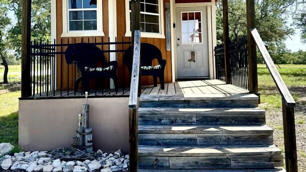 Un bâtiment en bois avec une enseigne indiquant « Wildbills Hideaway », une véranda avec des chaises et un escalier menant à l’entrée.
