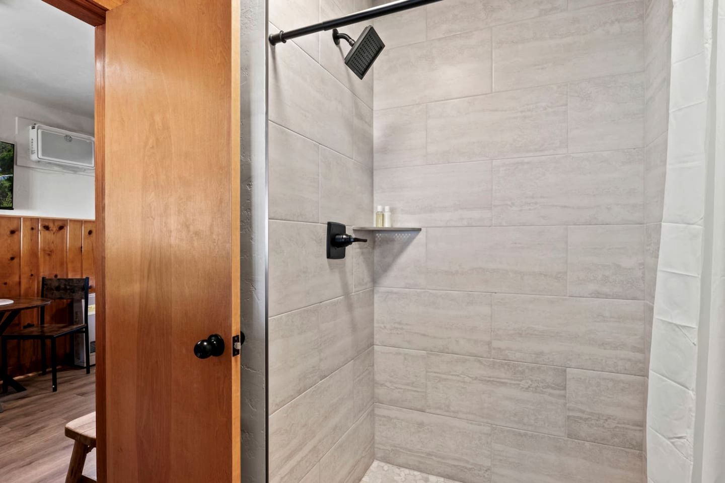A shower area with a tiled wall, a showerhead, and a shelf with toiletries.