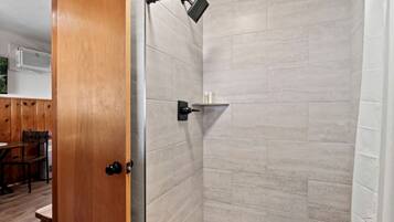 A shower area with a tiled wall, a showerhead, and a shelf with toiletries.