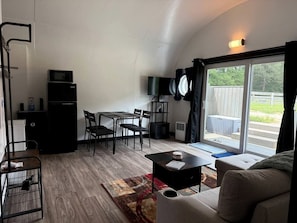 A compact living space with a dining area, a sofa, a TV, and a sliding glass door leading to an outdoor area.