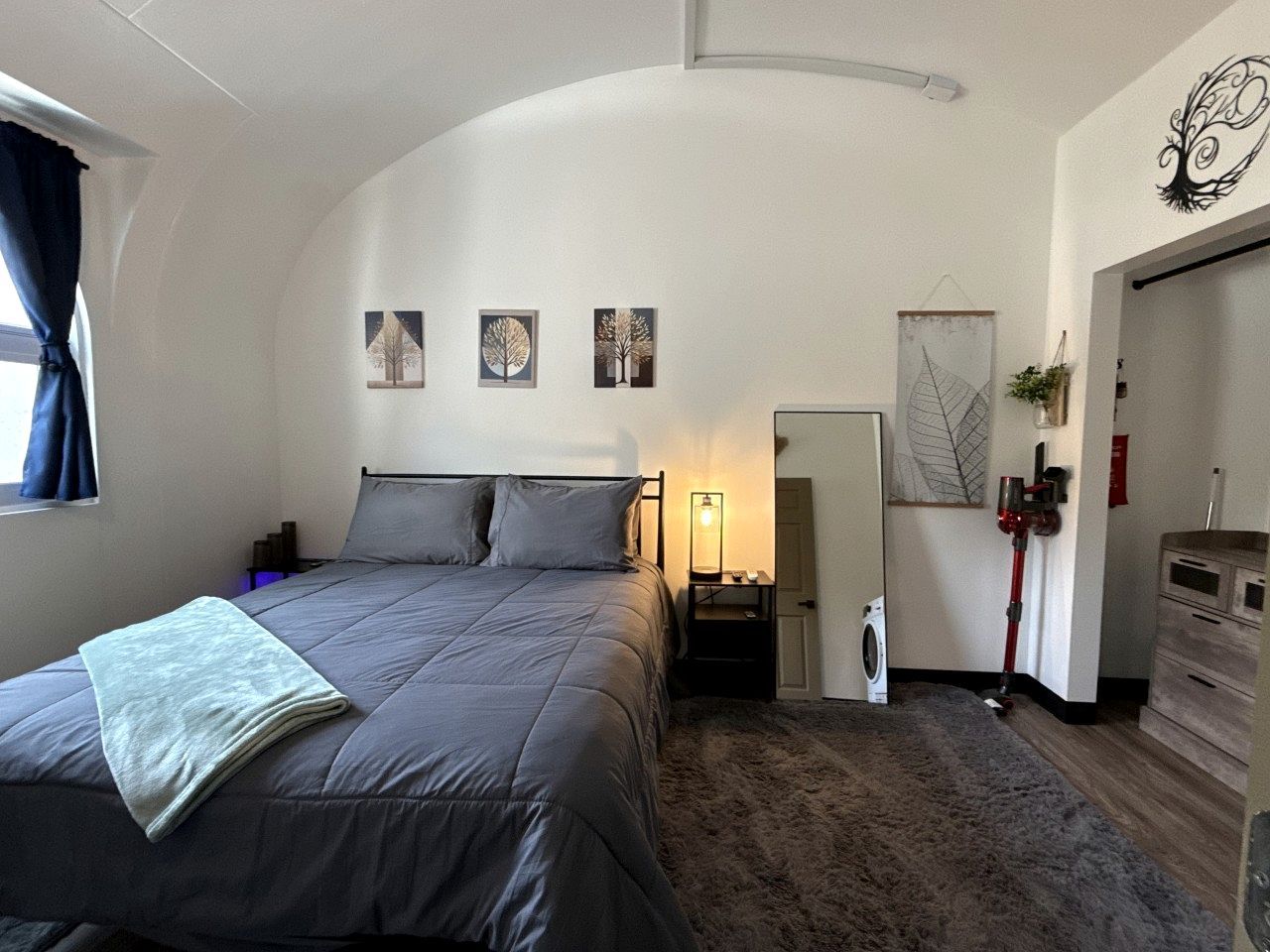 A bedroom with a bed, a nightstand, a dresser, a mirror, and wall art.