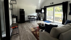A compact living space with a kitchenette, dining area, and seating by a large window. - Unique Earth Home Stay with Pet Goats and Fishing Pond near Lake Gaston NC (Littleton)