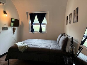 Une chambre à coucher comprenant un lit, une fenêtre avec des rideaux, un téléviseur à écran plat et des œuvres d’art accrochées au mur.