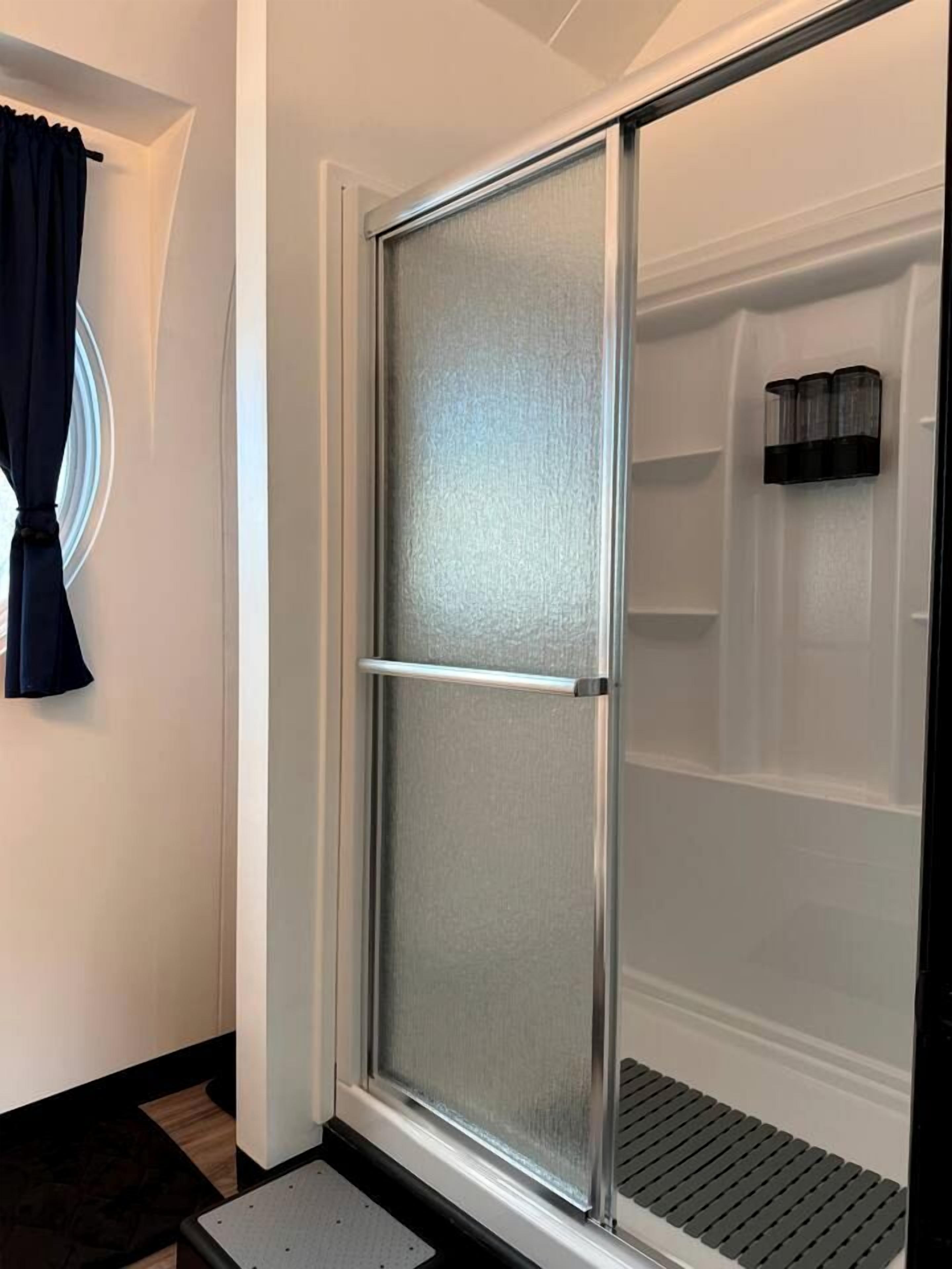 Una ducha con puerta de vidrio satinado, un toallero negro y un área de ducha blanca.