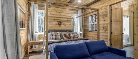 A wooden cabin interior with a bed, a blue sofa, a wooden bench, and a mounted deer head.
