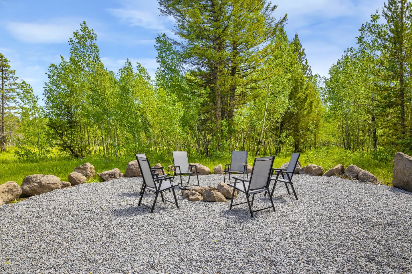 A gravel area with four chairs arranged in a circle, surrounded by rocks and trees.