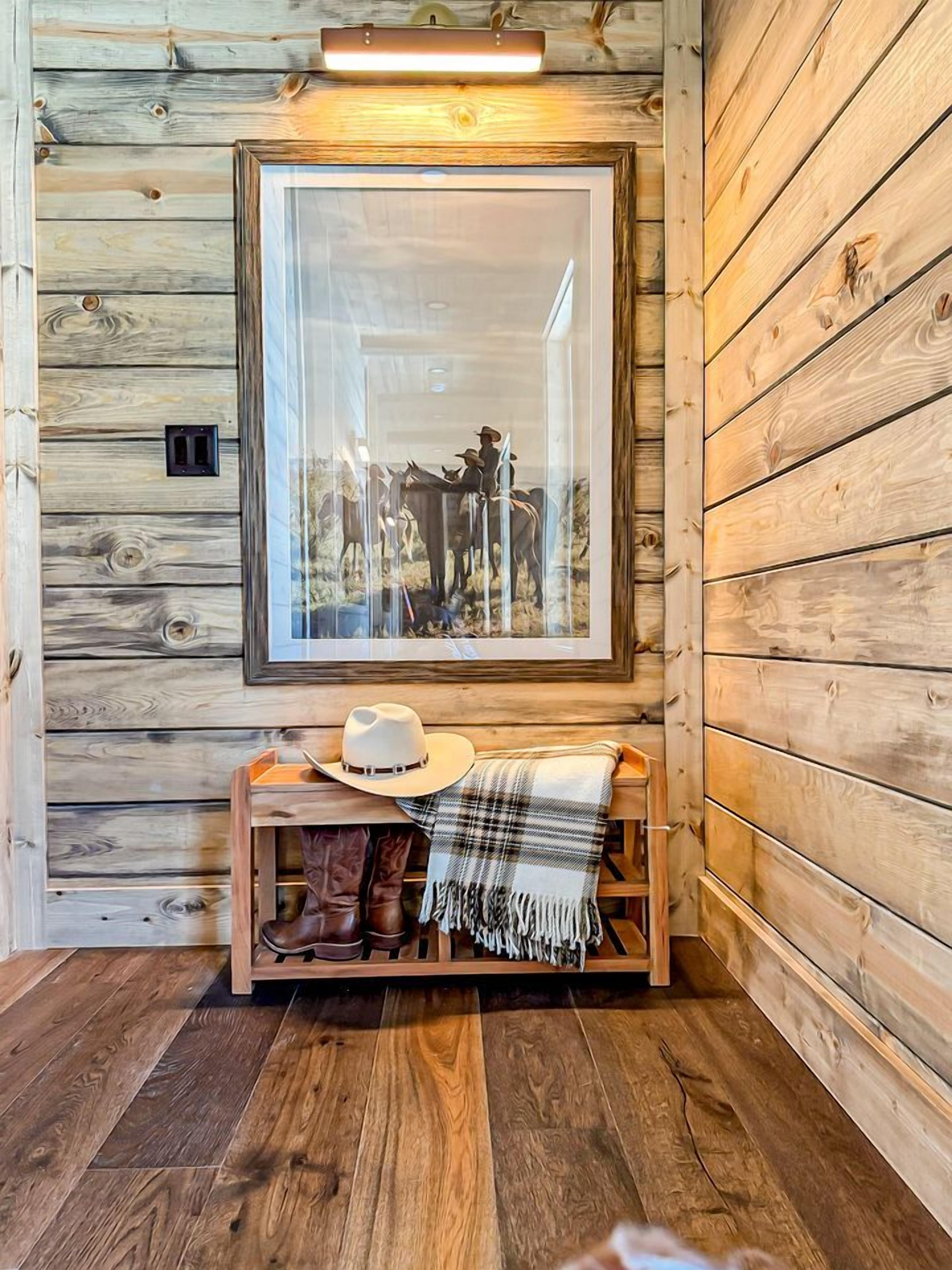 A wooden cabin interior with a framed picture, a hat, boots, and a plaid blanket on a wooden bench.