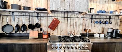 A kitchen with a stove, oven, hanging pots, and a wooden wall.