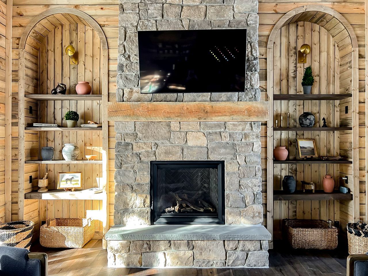 A stone fireplace with a television above it, wooden shelves with decorative items, and woven baskets on the floor.
