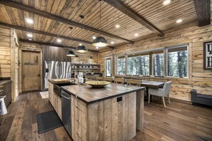 A log cabin interior with a central island, wooden walls, large windows, and a dining area. - Designed Rental with Awesome Indoor Spaces in Idaho (Island Park)