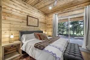 A wooden cabin bedroom with a bed, bedside lamps, and a view of the outdoors. - Designed Rental with Awesome Indoor Spaces in Idaho (Island Park)