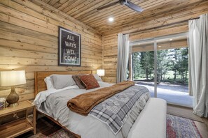 Ein Schlafzimmer einer Holzhütte mit Bett, Kissen, einem Nachttisch, einem gerahmten Schild und Blick ins Freie.