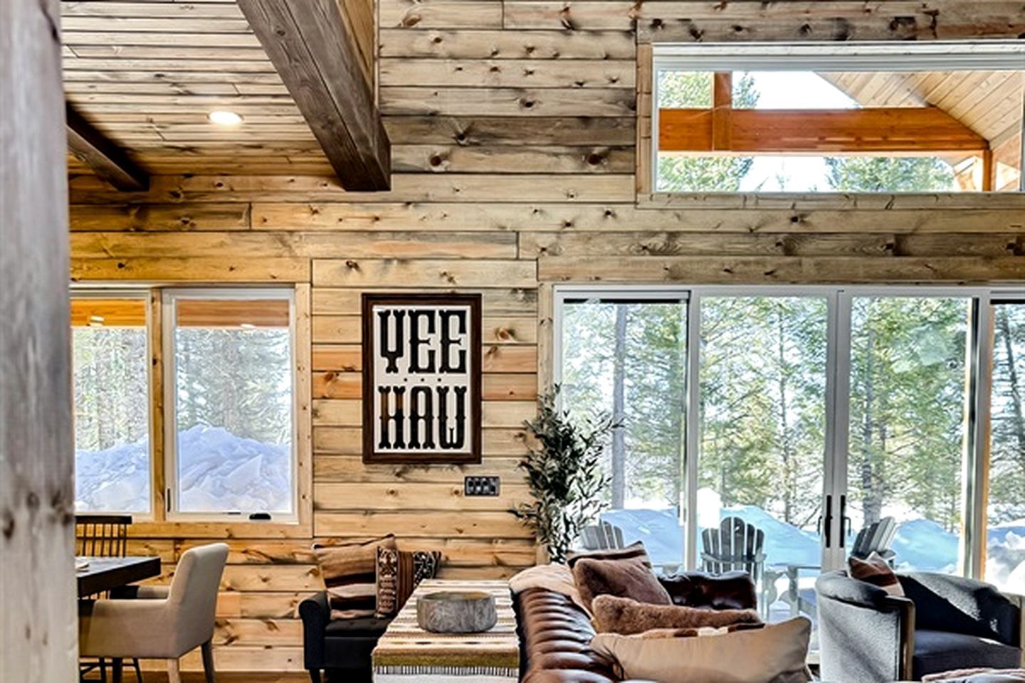 A log cabin interior with a large window, a framed sign, and a cozy seating area.