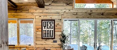 A log cabin interior with a large window, a framed sign, and a cozy seating area.