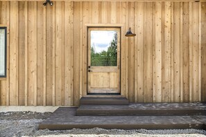A wooden building with a central door, a small outdoor area with steps, and a lamp on the wall. - Designed Rental with Awesome Indoor Spaces in Idaho (Island Park)