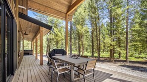 A covered outdoor deck with a table and chairs, surrounded by a forest. - Designed Rental with Awesome Indoor Spaces in Idaho (Island Park)