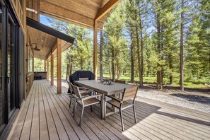 Eine überdachte Holzterrasse mit Tisch und Stühlen, umgeben von einem Wald.