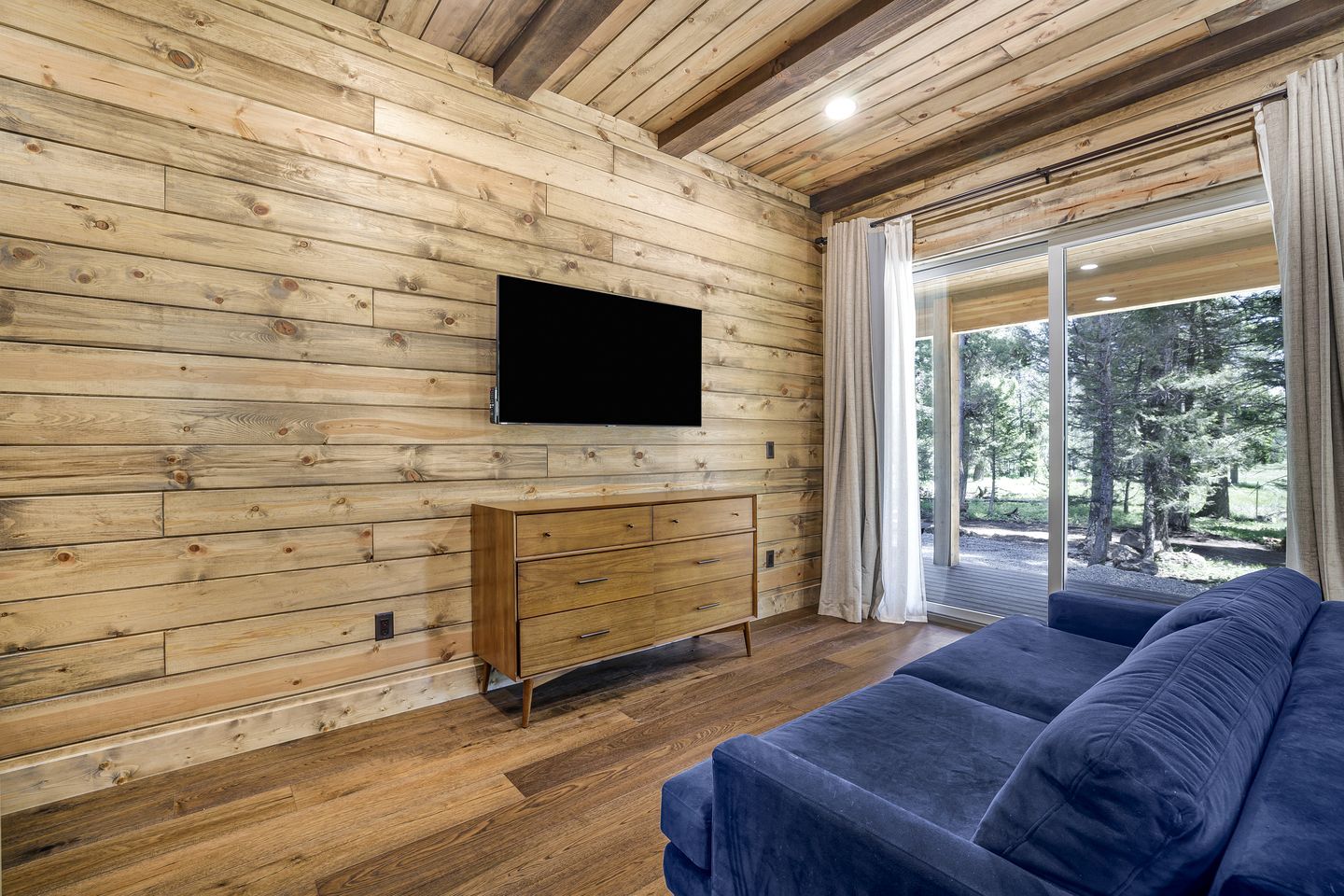 Een kamer met houten lambrisering, een bank, een aan de muur bevestigde televisie en een schuifdeur van glas die leidt naar een buitenruimte.