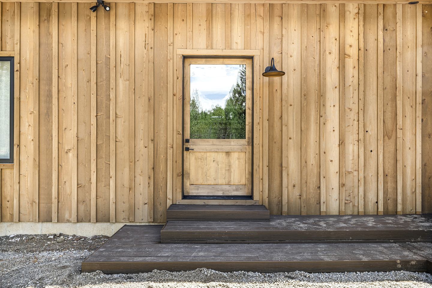 A wooden building with a central door, a small outdoor area with steps, and a lamp on the wall.