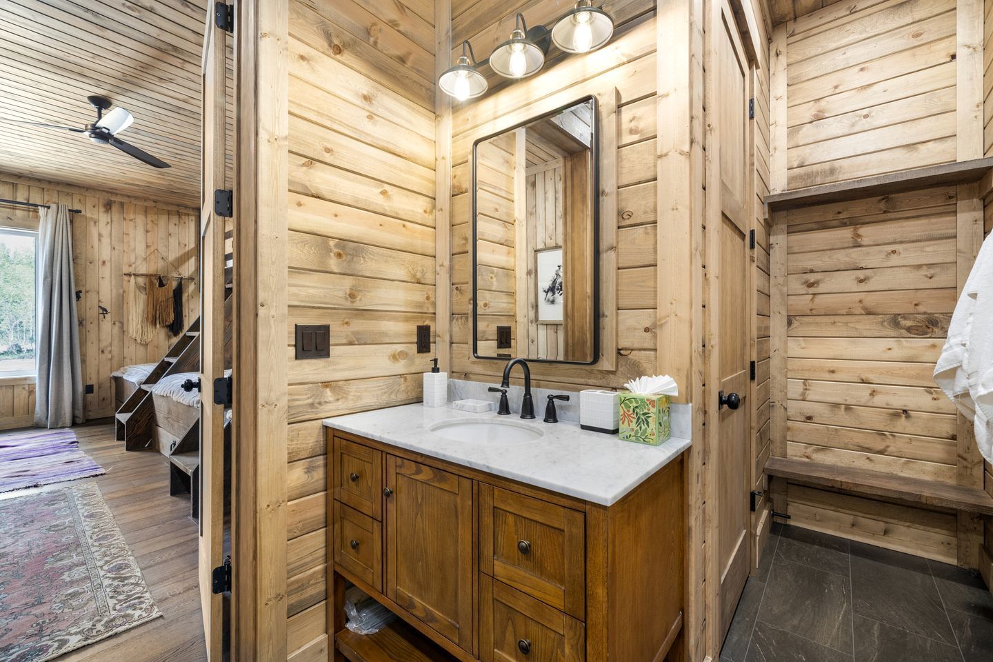 A wooden cabin interior with a bathroom featuring a sink, mirror, and wooden cabinets.
