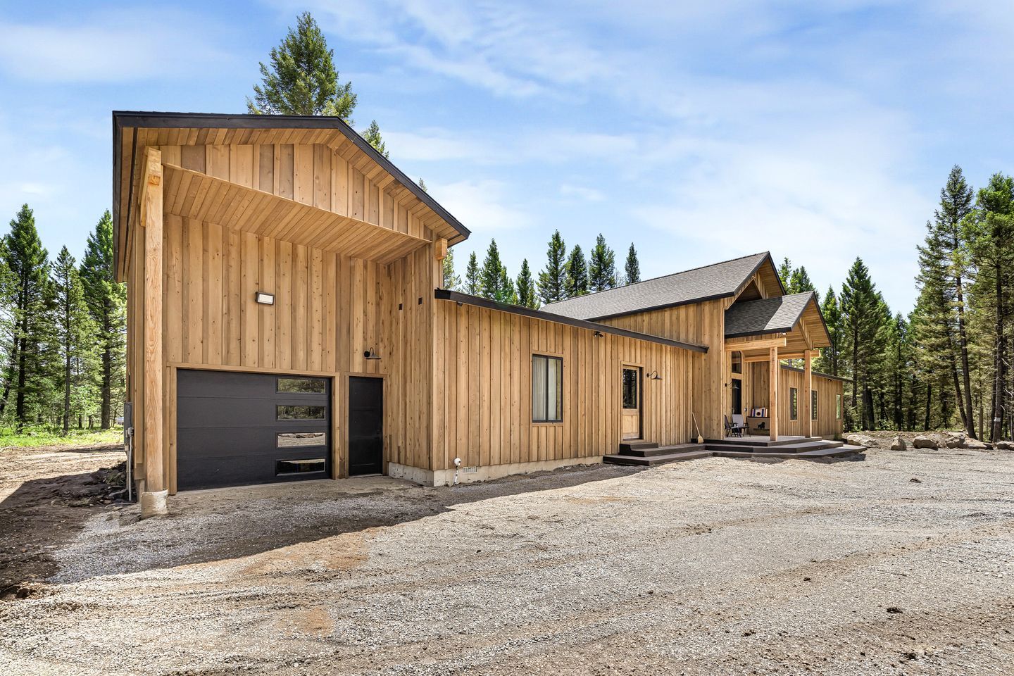 A wooden cabin with a garage, a covered porch, and a gravel driveway.