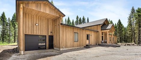 A wooden cabin with a garage, a covered porch, and a gravel driveway.