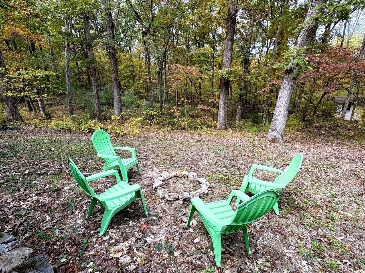Ein bewaldetes Gebiet mit drei grünen Adirondack-Stühlen, die um eine Feuerstelle aus Stein angeordnet sind.