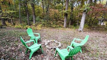 Ein bewaldetes Gebiet mit drei grünen Adirondack-Stühlen, die um eine Feuerstelle aus Stein angeordnet sind.