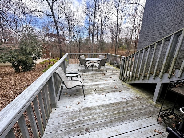 A wooden deck with a railing, a table with chairs, and a view of trees and a building.