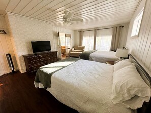 Ein Hotelzimmer mit zwei Betten, einem Schminktisch, einem Fernseher und einem Deckenventilator.