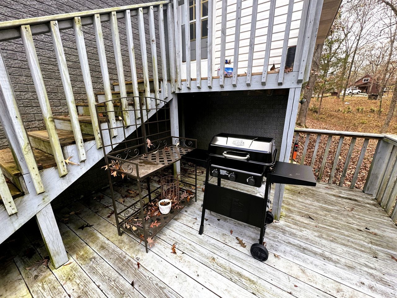 A barbecue grill on a wooden deck with a metal rack and a white pot.