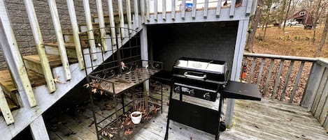 A barbecue grill on a wooden deck with a metal rack and a white pot.