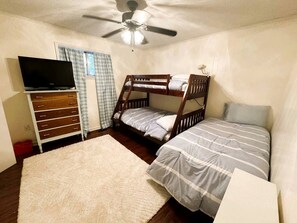 A bedroom with a bunk bed, a television on a dresser, a ceiling fan, and a window with curtains.
