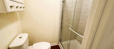 A bathroom with a toilet, a shower enclosure, and a cabinet with drawers.