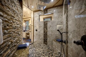 A stone-walled bathroom with a shower, a sink, and a mirror. - Woodland Romance (Broken Bow)