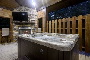 A hot tub with a stone fireplace and a TV mounted on a stone wall. - Woodland Romance (Broken Bow)
