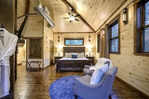 A log cabin bedroom with a bed, a chair, a small table, and a window. - Woodland Romance (Broken Bow)