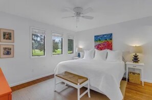 Une chambre Ă coucher avec un lit, un banc, un ventilateur de plafond, une fenĂȘtre et un tableau.