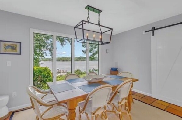 Un espace repas comprenant une table et des chaises, un luminaire suspendu et une vue dĂ©gagĂ©e sur lâextĂ©rieur grĂące Ă de grandes fenĂȘtres.