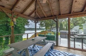 A covered outdoor area with a wooden deck, picnic table, and benches. - Riverfront Retreat: Hot Tub, Fire Pit, Private Dock & Screened Porch (Lancaster)
