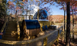 A wooden deck with a barbecue grill, a dome-shaped structure, and a staircase leading to a covered area.