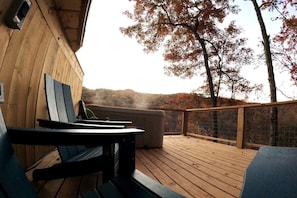 A wooden deck with a view of autumn trees, a chair, and a table.