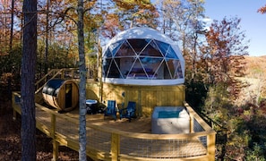 A geodesic dome structure with a deck, seating, and a hot tub.