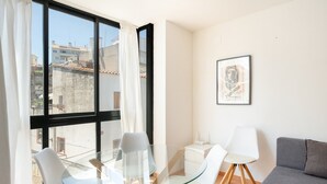 Ein modernes Wohnzimmer mit Glastisch, weißen Stühlen, einem grauen Sofa und einem gerahmten Bild an der Wand.