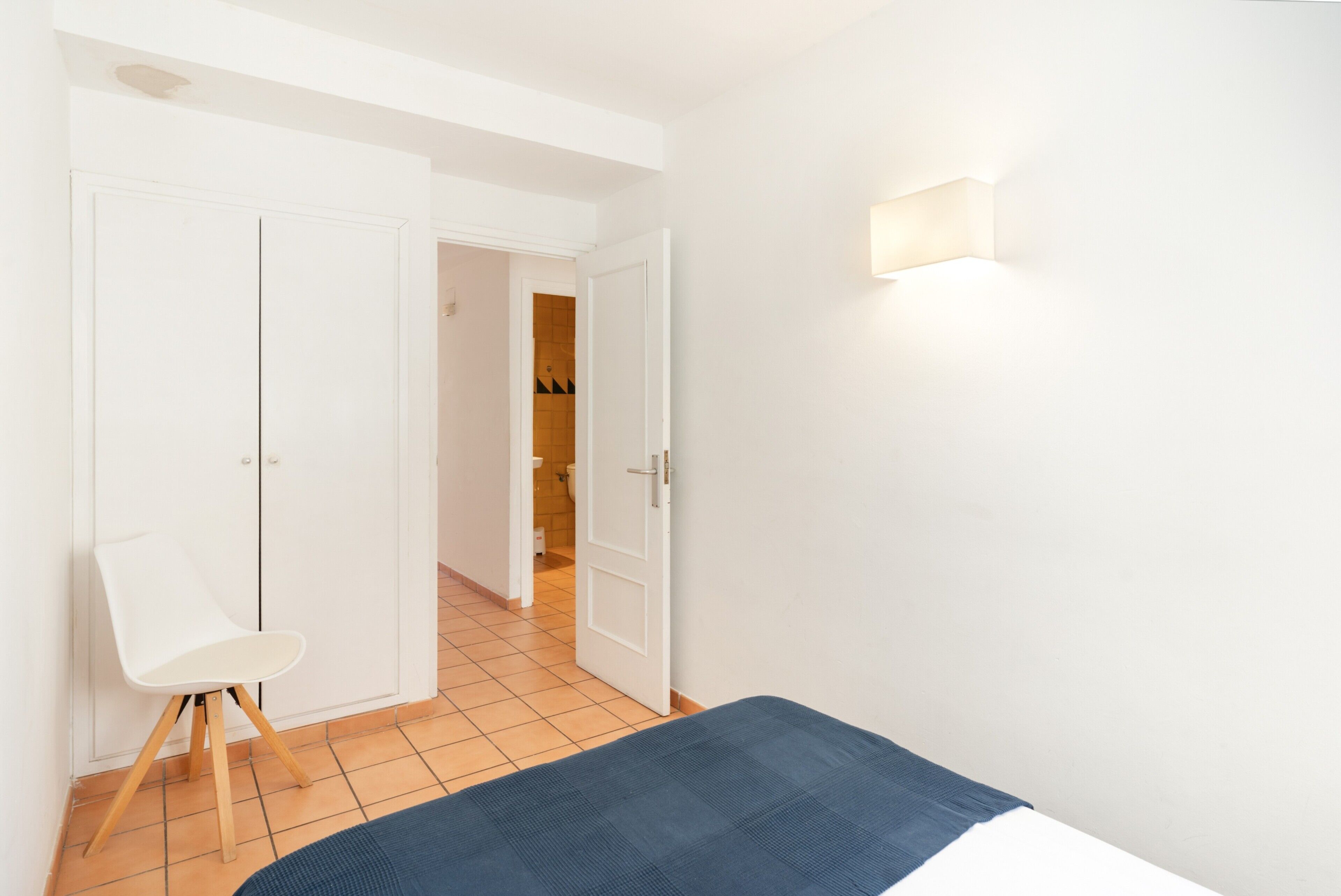 A bedroom with a bed, a chair, and a door leading to a bathroom.